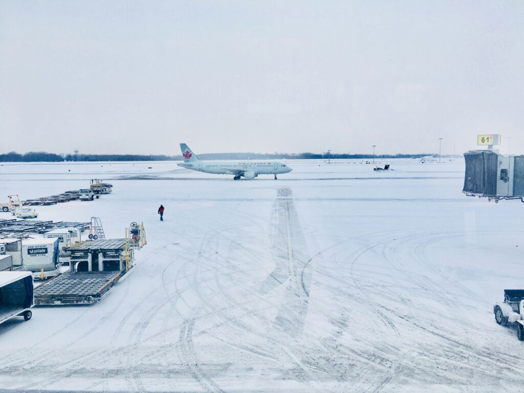 Snow-covered airport with planes on the tarmac and winter maintenance equipment in operation.